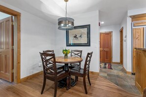 Een eetgedeelte met een ronde houten tafel, vier stoelen, een vaas met bloemen en een ingelijste foto aan de muur.