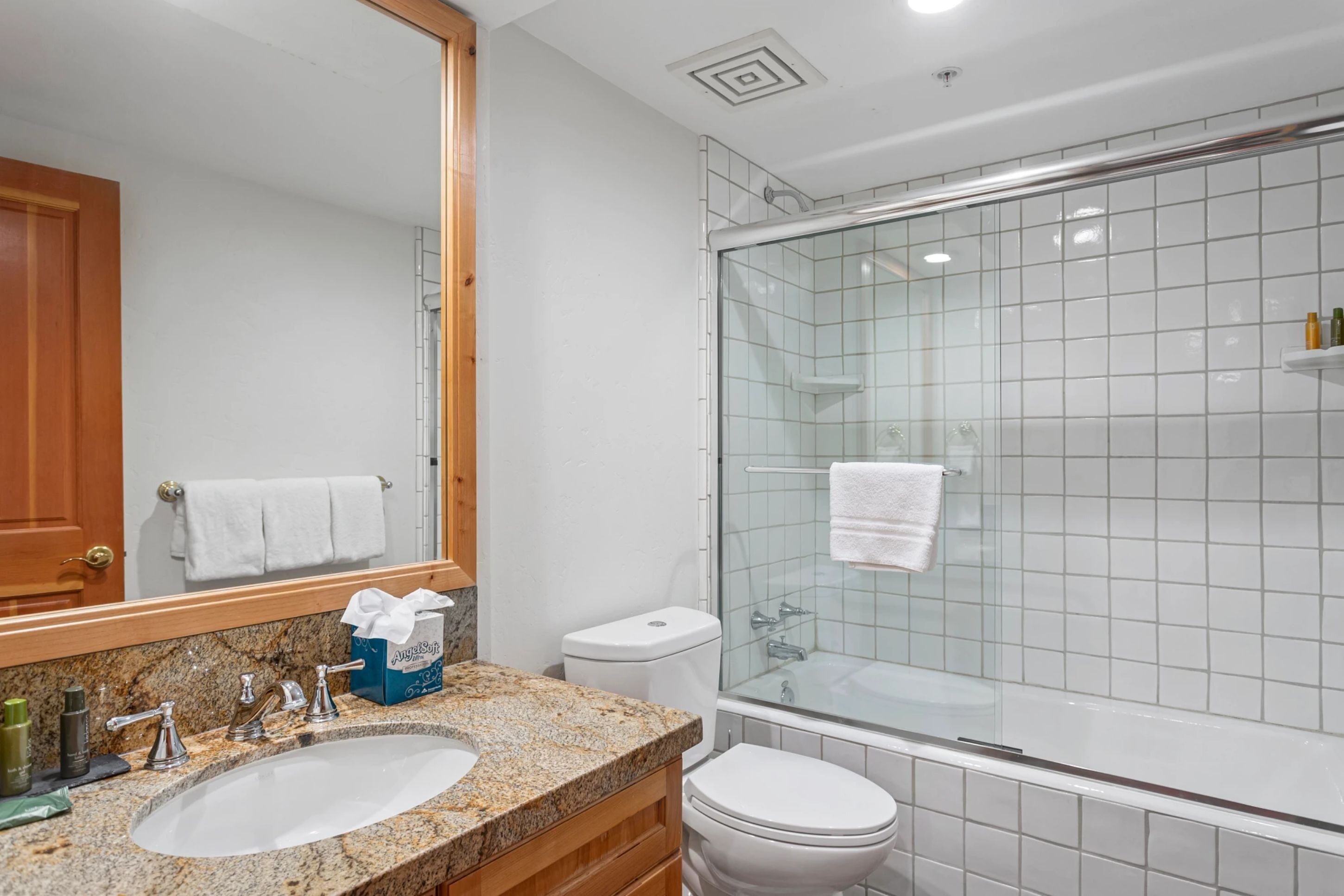 A bathroom with a granite countertop sink, a glass-enclosed shower, and a white toilet.