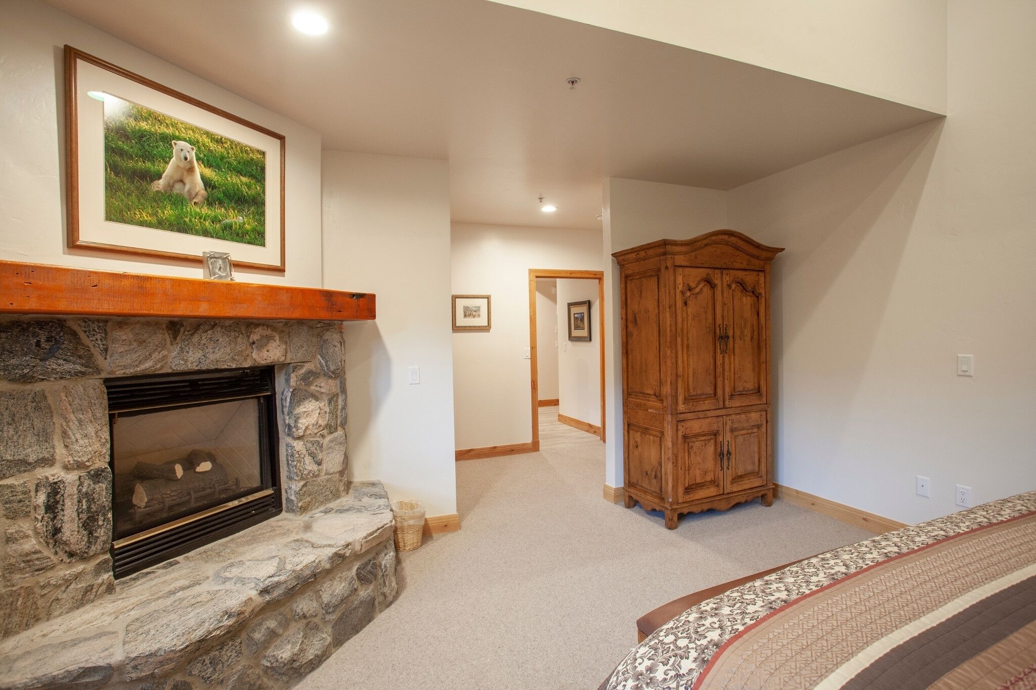A stone fireplace with a framed picture above it, a wooden cabinet, and a carpeted floor.