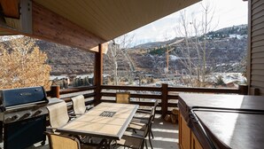 A covered outdoor patio with a grill, table, and chairs, overlooking a scenic valley with a view of a river and mountains. - Trail's End Lodge at Deer Valley Resort - Four Bedroom Residence with Space #504 4 Condo (Park City)