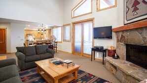 A spacious living room with a fireplace, a kitchen in the background, and a large window. - Trail's End Lodge at Deer Valley Resort - One Bedroom Residence with Spa #305 1 Condo (Park City)