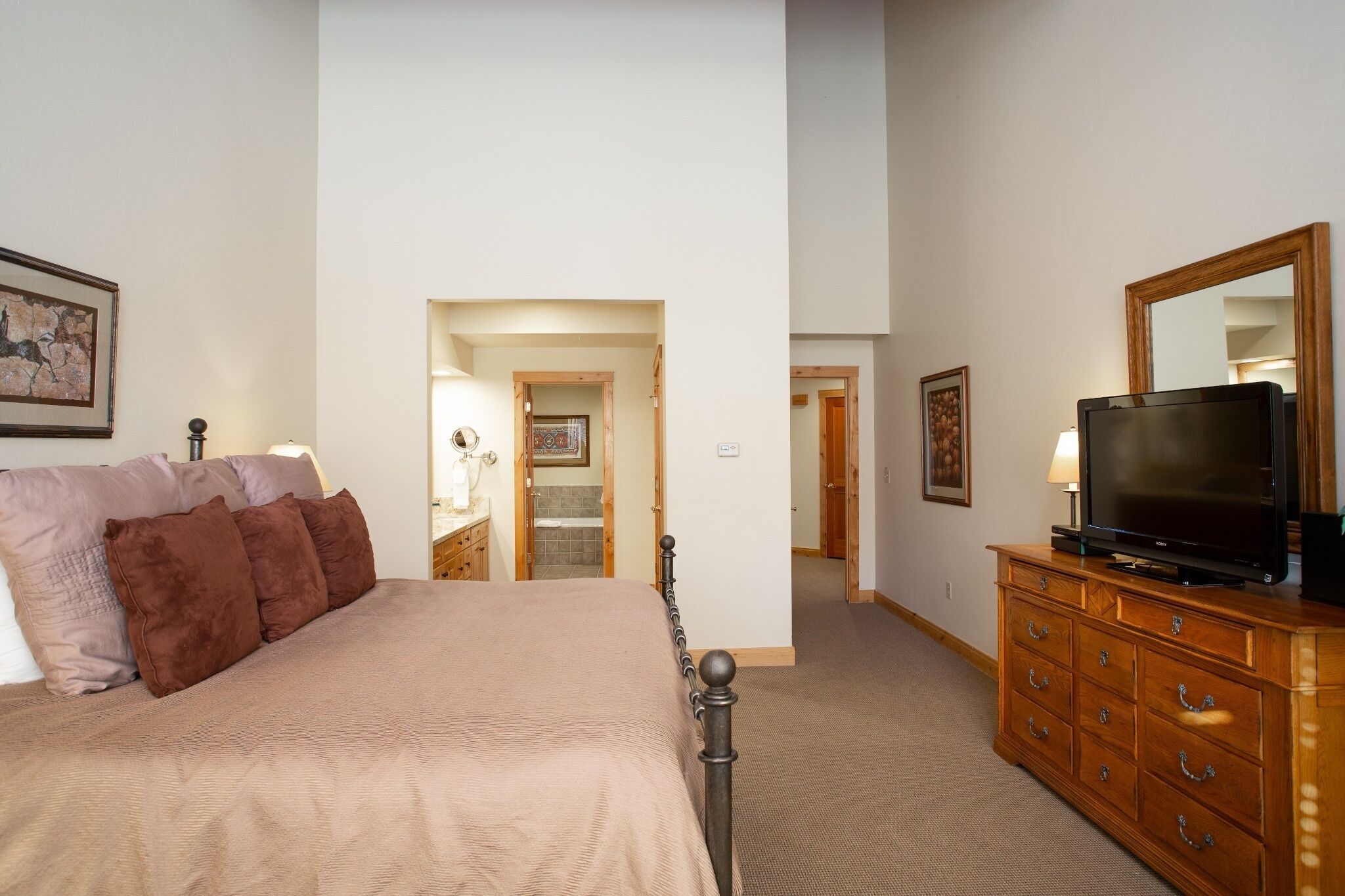 Un dormitorio con cama, cómoda, televisor y un pasillo que conduce a otra habitación.