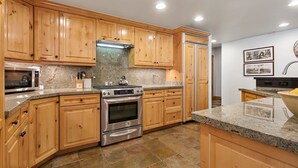 A kitchen with wooden cabinets, granite countertops, stainless steel appliances, and a tiled floor.