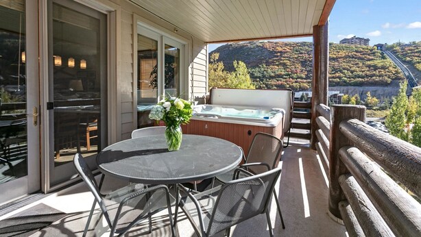 A covered outdoor area with a table and chairs, a hot tub, and a scenic view of a valley and mountains.