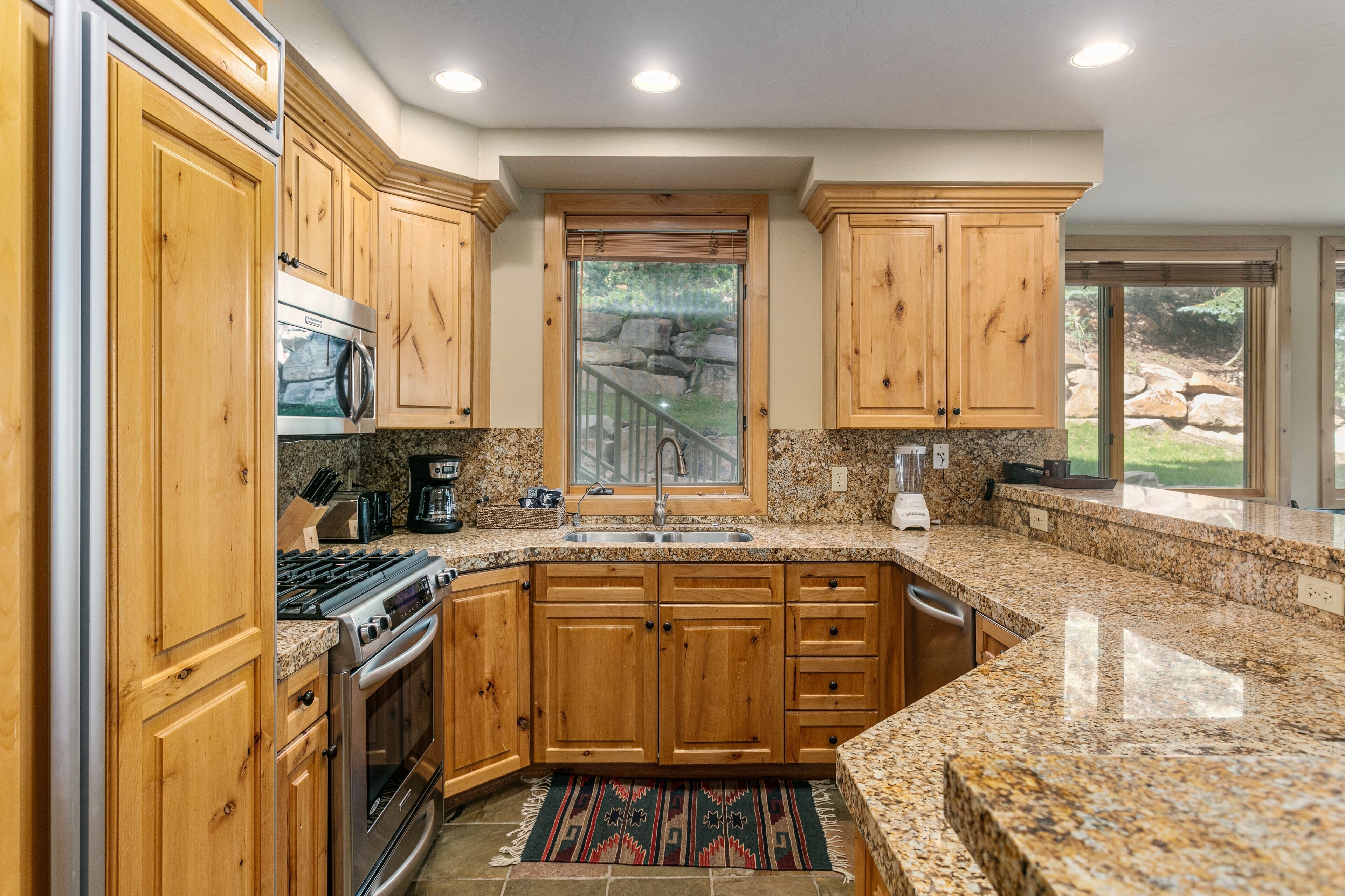 A kitchen with wooden cabinets, granite countertops, stainless steel appliances, and a view of a landscaped outdoor area.