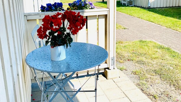 Un espace extérieur abrité, doté d’une table en métal et de bancs, entouré de bâtiments blancs avec des vérandas attenantes.
