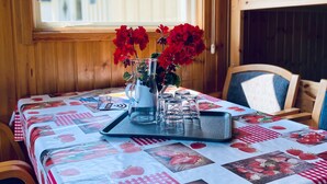 A wooden interior with a table set for dining, featuring a strawberry-themed tablecloth and a window with a wooden blind.