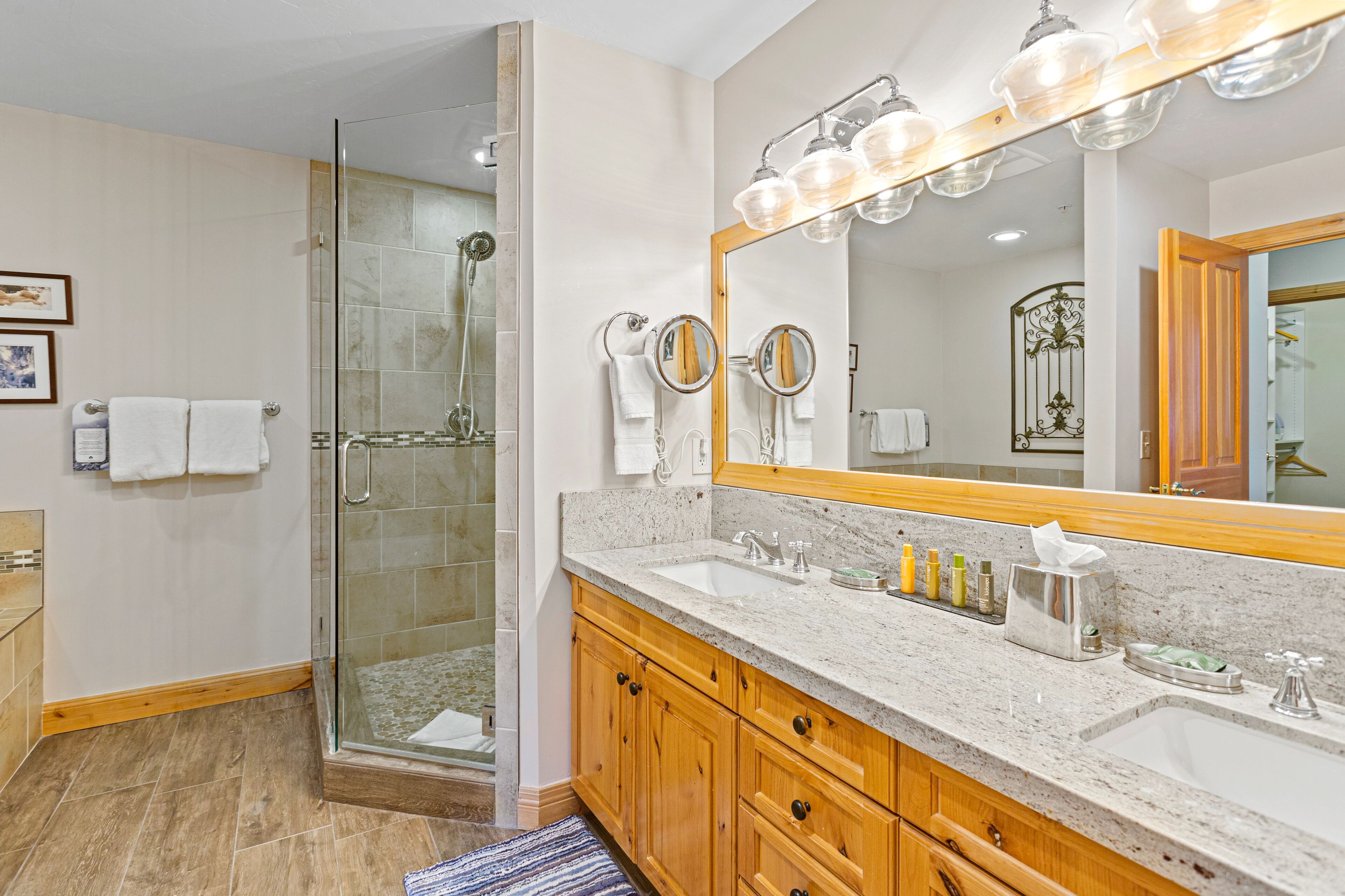 A modern bathroom with a glass-enclosed shower, a large vanity with a mirror, and a sink with toiletries.