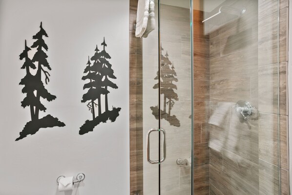 A bathroom with a glass shower door, a towel rack, and a wall decal of trees.