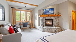 A cozy room with a stone fireplace, a bed, a desk with a chair, and a large window with curtains. - Trail's End Lodge at Deer Valley Resort - Two Bedroom Residence with Spa #404 2 Condo (Park City)