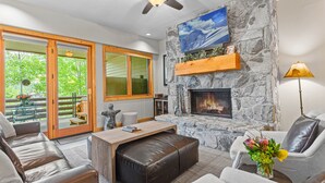 A spacious living room with a stone fireplace, comfortable seating, and a large window overlooking greenery. - Trail's End Lodge at Deer Valley Resort - Two Bedroom Residence with Spa #404 2 Condo (Park City)