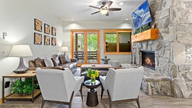 A living room with a stone fireplace, a ceiling fan, and a large window. - Trail's End Lodge at Deer Valley Resort - Two Bedroom Residence with Spa #404 2 Condo (Park City)