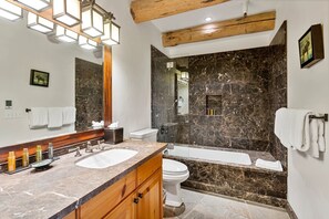 Un baño moderno con lavamanos de mármol, bañera y un espejo grande.