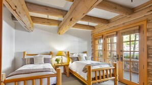 Une chambre dans un chalet en rondins, avec deux lits en bois, une table de chevet avec une lampe et une grande fenêtre donnant sur la forêt.