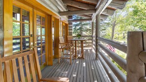 Une terrasse en bois avec une table et des chaises, une balustrade en bois et de grandes fenêtres.