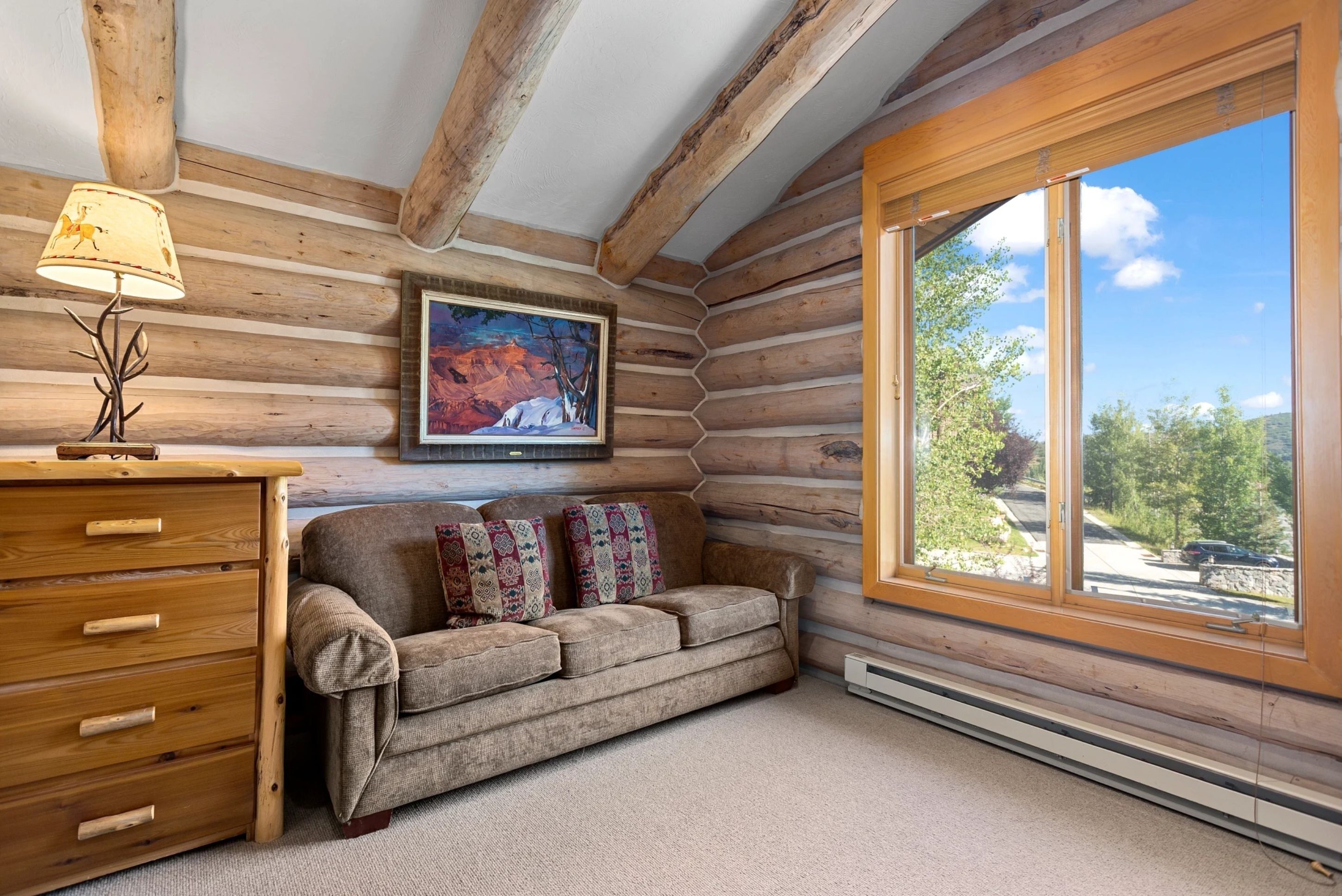 A log cabin interior with a sofa, wooden dresser, and a painting of a snowy landscape.