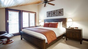 A bedroom with a wooden ceiling, a bed with a white and orange bedspread, two bedside lamps, and a nightstand with a lamp.
