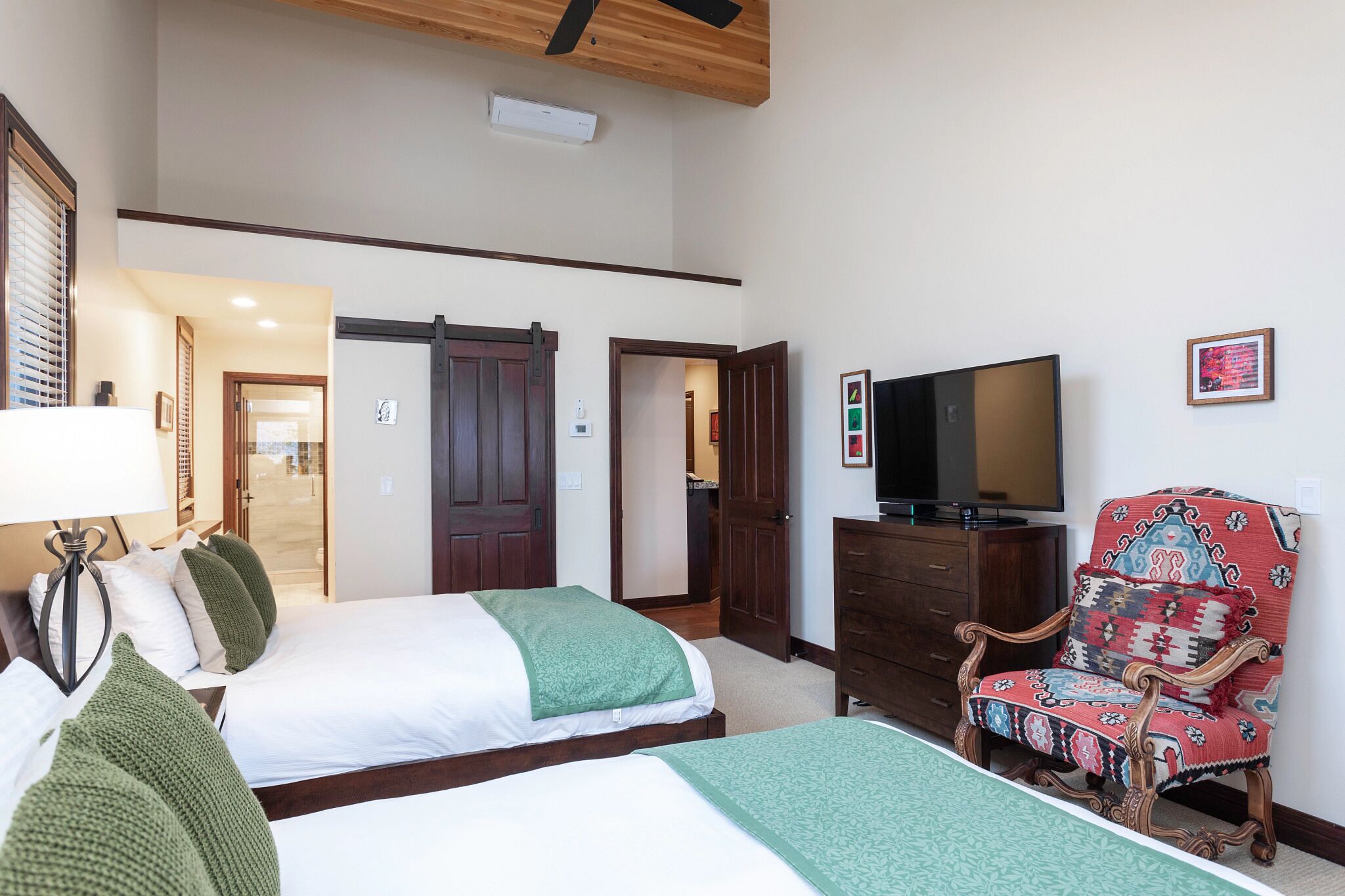 A hotel room with two beds, a TV, a wooden chair, and a door leading to another room.