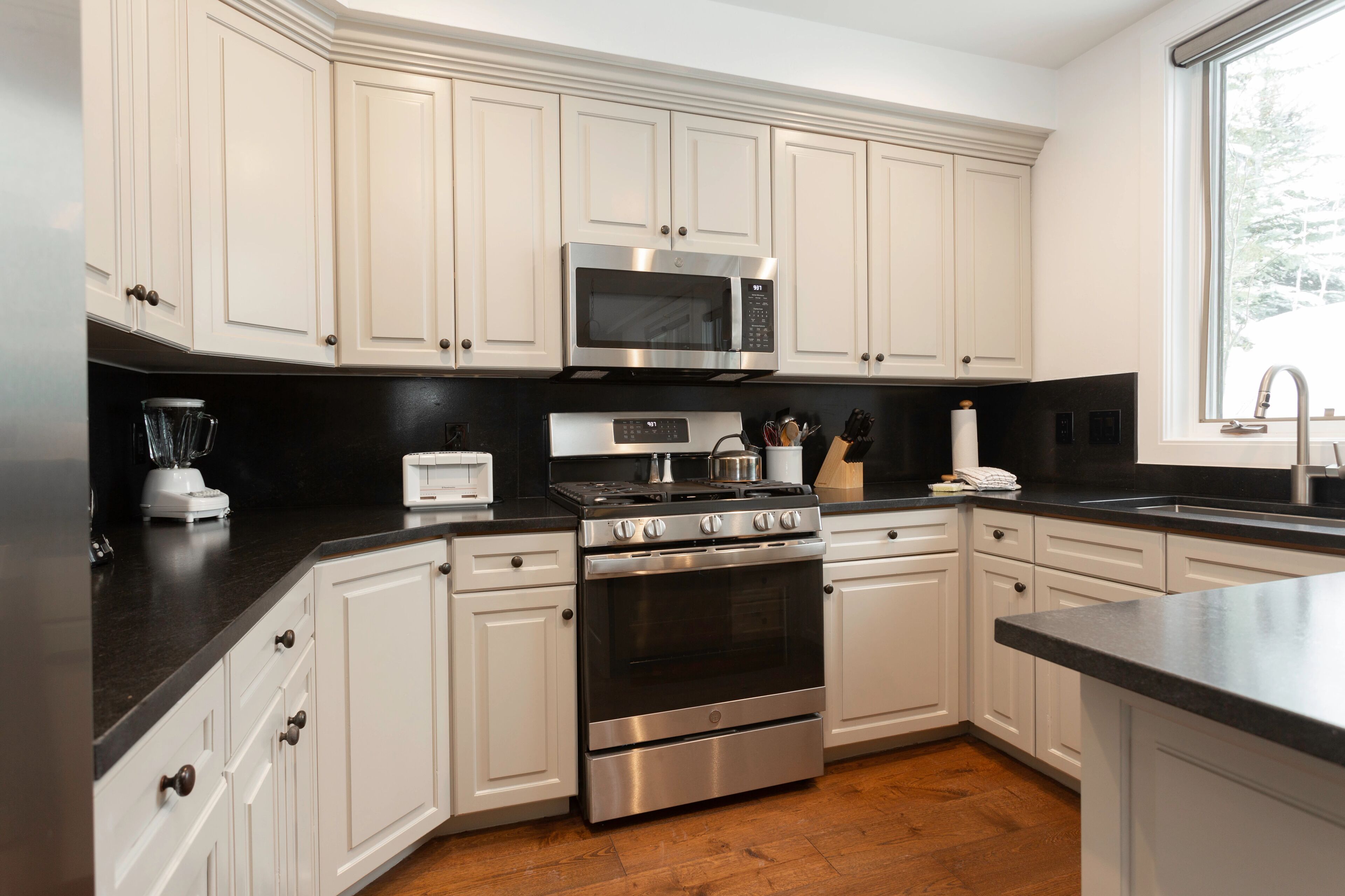 A modern kitchen with white cabinetry, a stainless steel stove, a microwave, and a black countertop.