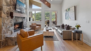 A modern living room with a stone fireplace, leather sofas, and a large window overlooking a scenic landscape. - Trail's End Lodge at Deer Valley Resort - Three Bedroom Residence with Spa #501 3 Condo (Park City)