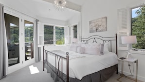 A bedroom with a large bed, a bedside table with a lamp, and a view of the outdoors through open shutters. - Trail's End Lodge at Deer Valley Resort - Three Bedroom Residence with Spa #501 3 Condo (Park City)