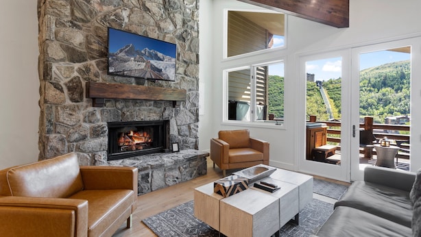 A cozy living room with a stone fireplace, leather sofas, and a large window offering a scenic view. - Trail's End Lodge at Deer Valley Resort - Three Bedroom Residence with Spa #501 3 Condo (Park City)