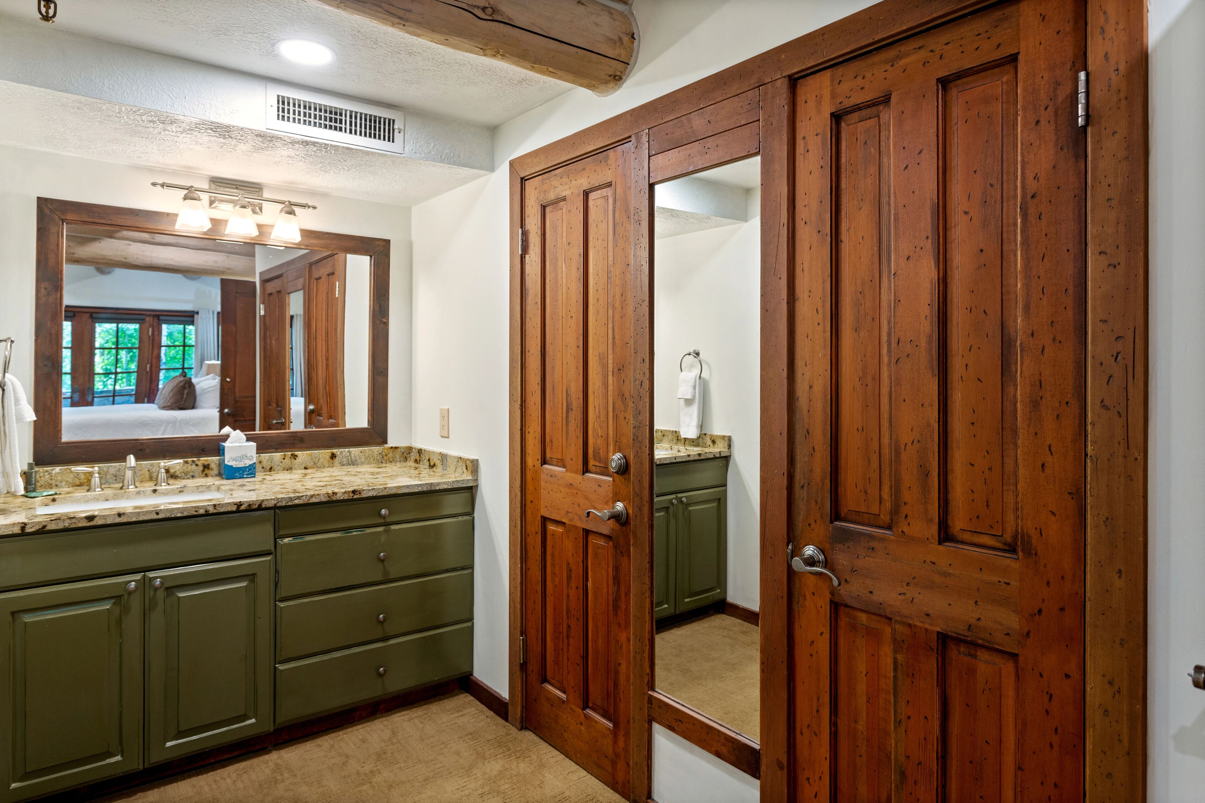 A bathroom with a wooden door, a sink with a mirror, and green cabinets.