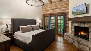A bedroom with a large bed, a stone fireplace, a chandelier, and a television on the wall.