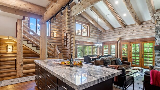 A log cabin interior with a kitchen island, dining area, and a staircase.