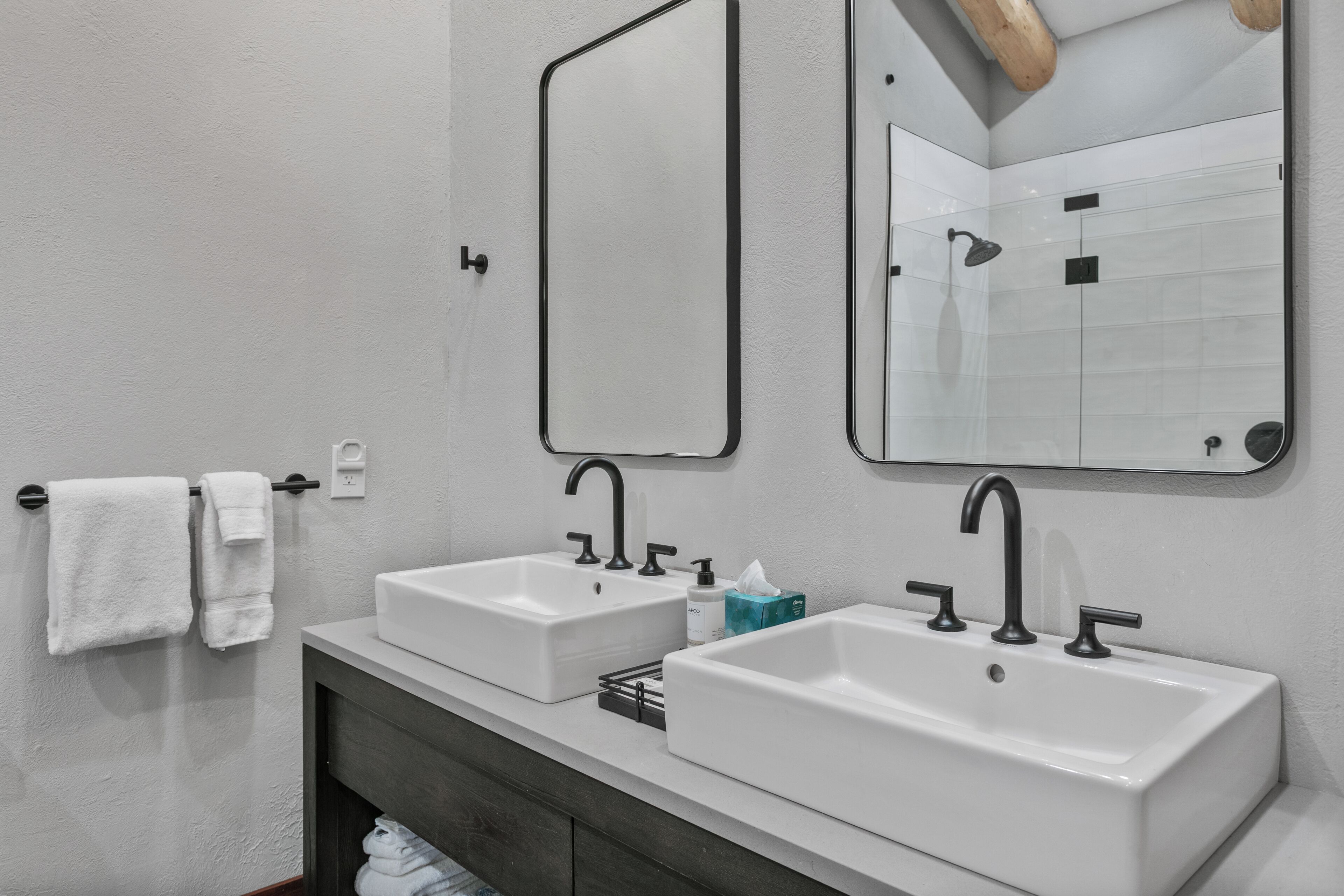 A modern bathroom with two white sinks, a dark vanity, and a large mirror.