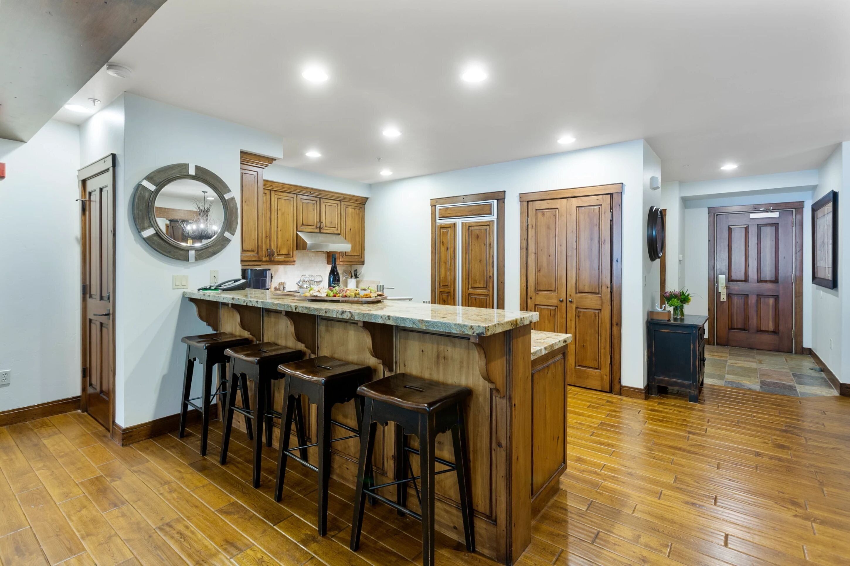 A kitchen with wooden cabinets, a central island with stools, and a large mirror.