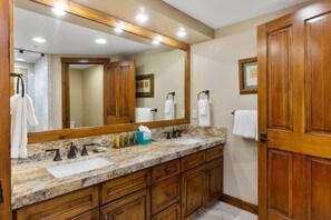 A bathroom with a granite countertop, wooden cabinets, a large mirror, and a door.
