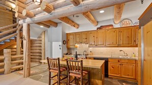 A rustic kitchen with wooden beams, a stone floor, and a bar area with stools.