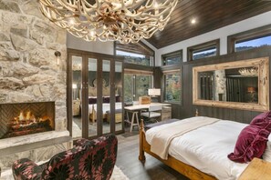 A bedroom with a stone fireplace, a large bed, a desk, and a view of the outdoors. - Trail's End Lodge - 4 Bedroom Condo Residence w/ Spa #13 by Deer Valley Resort (Park City)