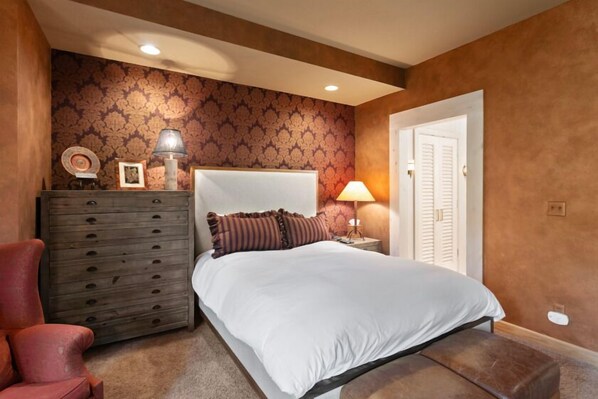 A bedroom with a large bed, a dresser, a chair, and a door. - Trail's End Lodge - 4 Bedroom Condo Residence w/ Spa #13 by Deer Valley Resort (Park City)