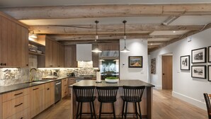 A kitchen with wooden cabinets, a stone backsplash, a central island with bar stools, pendant lighting, and a view into the dining area. - Pine Inn 9 - Two Bedroom Condo with Spa Trail's End Lodge by Deer Valley Resort (Park City)