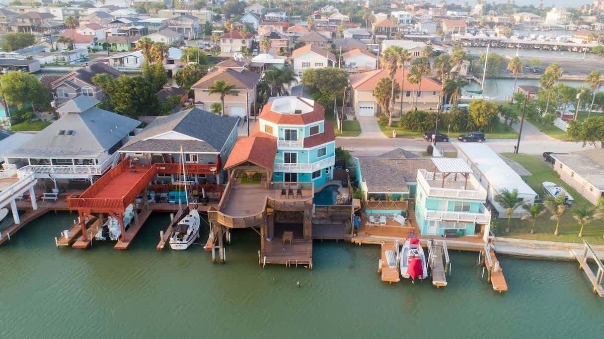 Um imóvel à beira-mar com vários barcos atracados, uma casa grande com um esquema de cores azul e branco característico e um pequeno barco-de-tesoura.