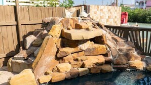 A rock formation by a pool with a wooden fence and a tiled wall in the background. - Blizzard's Lighthouse 4 Bedroom Home (Port Isabel)