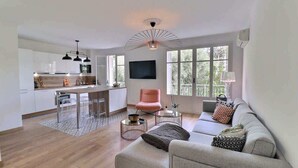 Een moderne woonkamer met een bank, een roze fauteuil en een eethoek met een televisie.