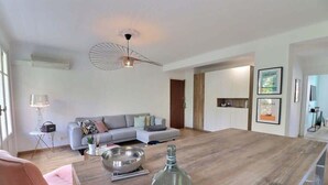 Een moderne woonkamer met een houten eettafel, een roze stoel, een bank en een bijzondere plafondlamp.
