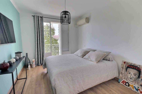 A bedroom with a bed, a desk, a chair, a hanging light fixture, and a window with curtains.
