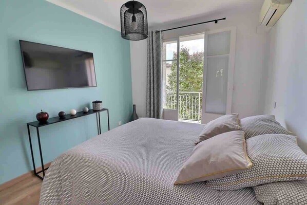 Un dormitorio con cama, televisor, una consola decorativa y un balcón con vistas.