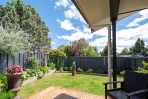 A patio with a wooden deck, a covered seating area, and a garden with various plants and a wooden fence. - Inn McDowell - Modern 3-Bed, Minutes to Te Puia (Rotorua)