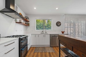 A modern kitchen with white cabinets, a gas stove, a dishwasher, and a window with blinds.