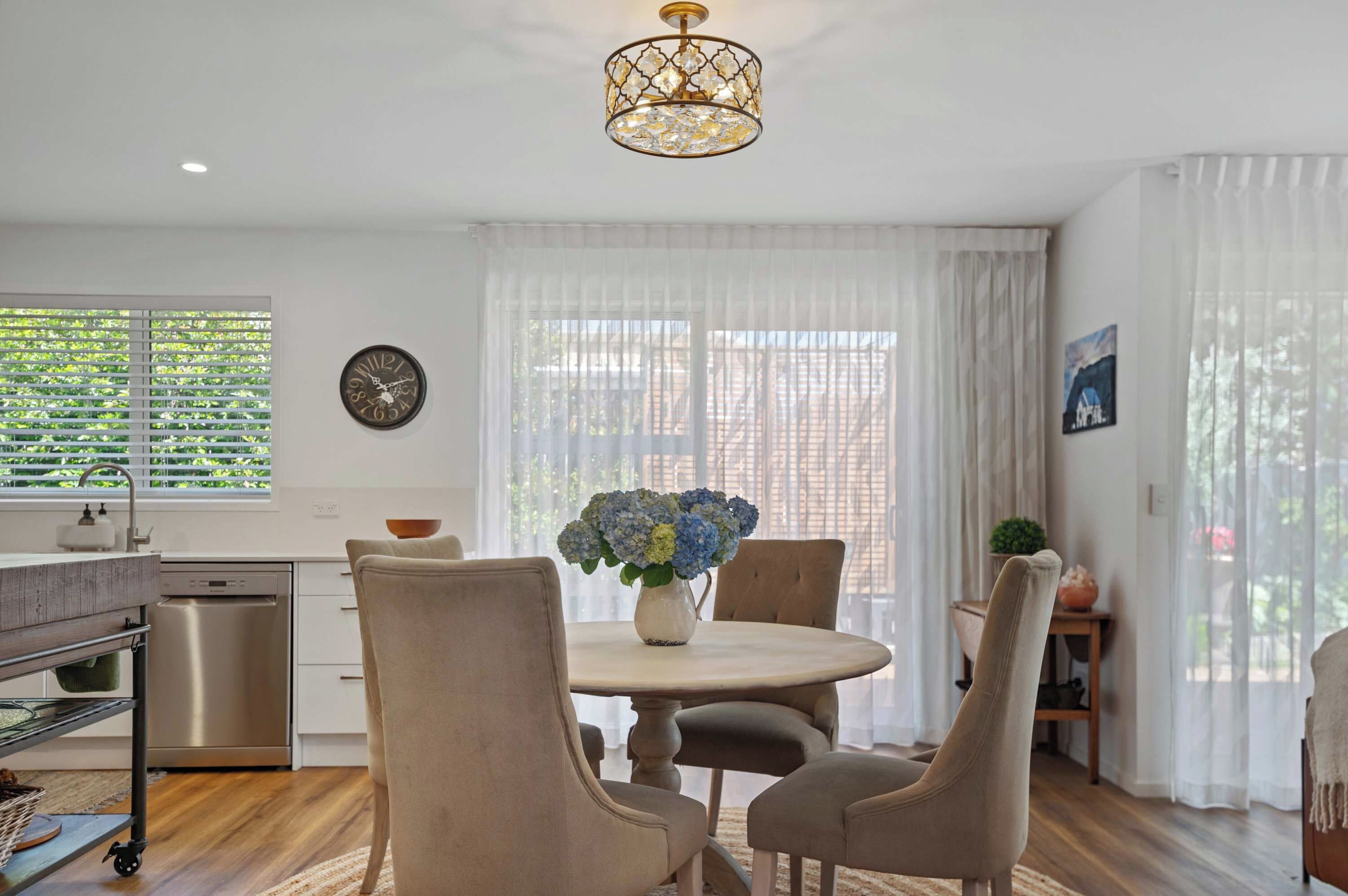 A modern kitchen with a dining area, featuring a round table, chairs, a chandelier, and a clock on the wall.