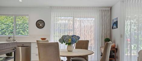 A modern kitchen with a dining area, featuring a round table, chairs, a chandelier, and a clock on the wall.