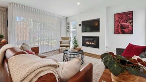 A living room with a fireplace, a sofa, a coffee table, and a large window with sheer curtains. - Inn McDowell - Modern 3-Bed, Minutes to Te Puia (Rotorua)