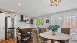 A modern kitchen with a stainless steel refrigerator, a wooden dining table with chairs, and a large window with blinds. - Inn McDowell - Modern 3-Bed, Minutes to Te Puia (Rotorua)