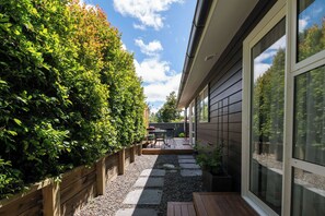 A patio with a table and chairs, a wooden fence, and a gravel path leading to a house with large windows. - Inn McDowell - Modern 3-Bed, Minutes to Te Puia (Rotorua)