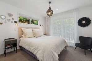 A bedroom with a bed, bedside table, and a chair. - Inn McDowell - Modern 3-Bed, Minutes to Te Puia (Rotorua)